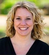 A white woman with blonde hair is wearing a black v-neck shirt. The picture is head-and-shoulders.